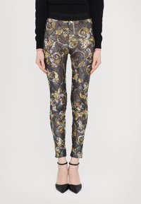 Glitrende, tettsittende leggings har et flerfarget, utsmykket mønster med gullakenter og en svart elastisk midjebånd. Vist med svarte hæler.