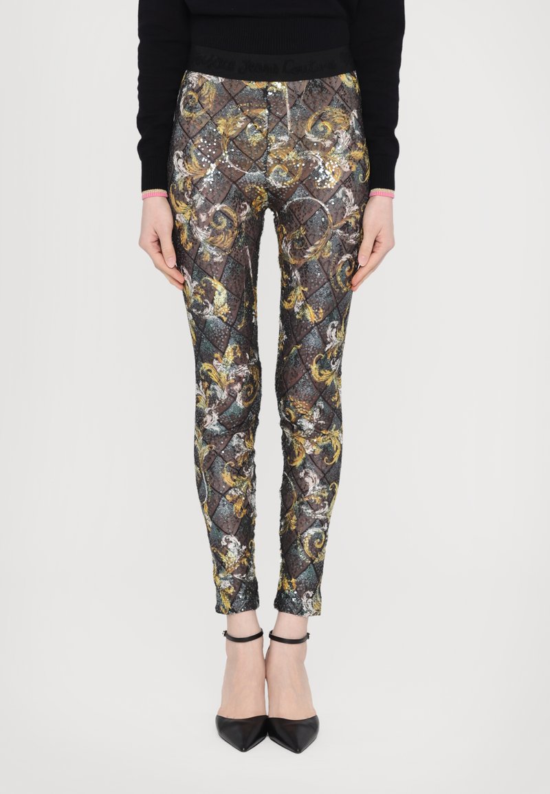 Glitrende, tettsittende leggings har et flerfarget, utsmykket mønster med gullakenter og en svart elastisk midjebånd. Vist med svarte hæler.