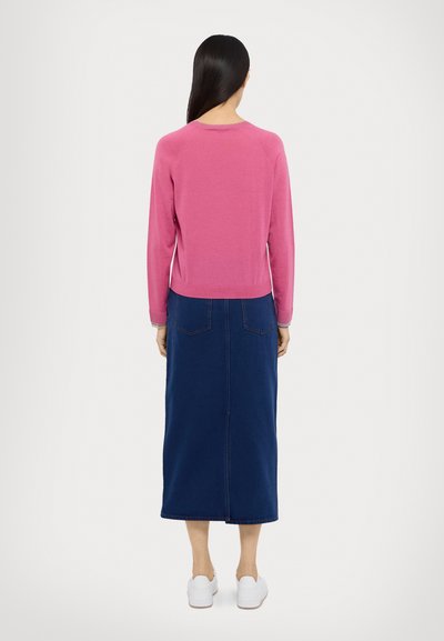 Suéter rosa de mangas longas combinado com uma saia de ganga azul escura, com corte reto e bolsos traseiros. Acompanhado por ténis brancos.