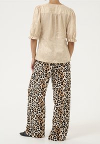 Blusa beige lucida con maniche a sbuffo abbinata a pantaloni larghi con stampa leopardata in tonalità marroni e nere. Scarpe nere basse visibili.