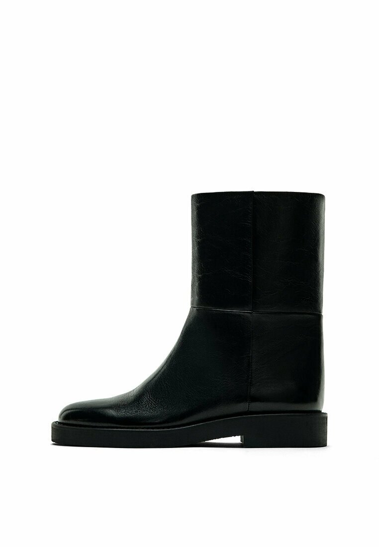 Black leather ankle boot with a smooth texture, square toe, and a flat rubber sole. Features a sleek, minimalist design and no visible hardware.