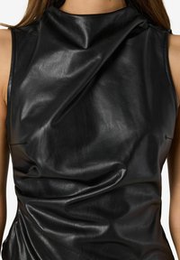 Svart läderoberdel med hög krage, med en slät textur och mjukt fall, som framhäver unika veck och skräddarsydda sömmar.