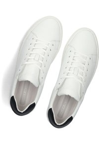 White leather sneakers with black heel accents, flat laces, rounded toe, and textured inner lining. Minimalist design with subtle branding.