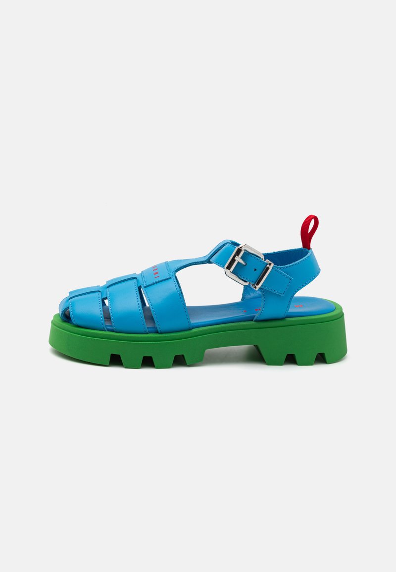 Sandală sintetică albastră cu talpă chunky verde, având un design cu curea, cataramă ajustabilă și un bucluc roșu în spate pentru a fi ușor de purtat.