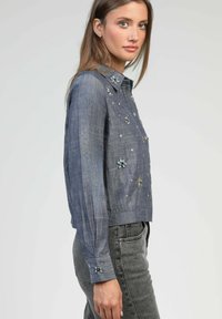 Chemise en denim courte, tissu bleu clair, détails floraux brodés, poignets à boutons, col, design court, tissage texturé.