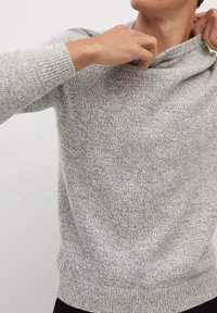 Pull en maille grise avec un motif texturé, doté d'un col en cowl et de poignets et un ourlet côtelés. Le tissu semble doux et confortable.