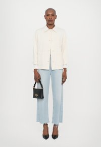 Light cream button-up jacket, light blue wide-leg distressed jeans, black handbag with twisted handle, and black pointed-toe heels.