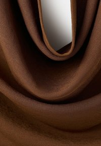 Tissu marron en maille drapé et plié pour montrer la texture et l'élasticité, mettant en valeur les caractéristiques d'un matériau doux et lisse.