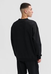 Svart sweatshirt med avslappnad passform, rund hals och ribbade ärmslut. Slät tygliknande struktur utan synliga mönster eller logotyper.