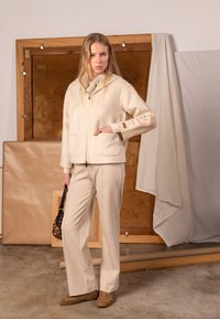 Beige zip-up hoodie med framlår, ribbade muddar och ylleliknande textur, kombinerad med beige byxor och en leopardmönstrad väska.