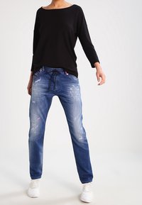 Top negro de manga larga combinado con jeans de mezclilla azules holgados que presentan detalles desgastados y una cintura con cordón, complementado con zapatillas blancas.