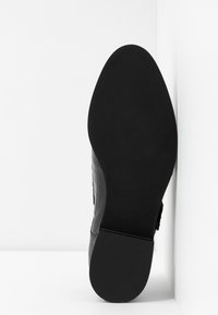 Chaussure en cuir noir avec semelle lisse et petit talon bloc, montrée avec la semelle face vers l'avant sur fond blanc.