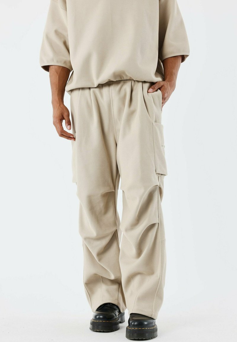 Pantalons cargo beiges à coupe ample, fabriqués en tissu doux, avec des poches latérales et une taille à cordon, associés à des bottes noires épaisses.