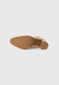 Scarpa in suede beige con punta tondeggiante, dotata di una suola in gomma marrone liscia e un logo sottile impresso sul lato.