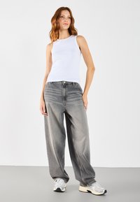 Hvit ribbet tanktop kombinert med vide grå bukser og grå sneakers. Antrekket har et enkelt design og er behagelig å bruke.