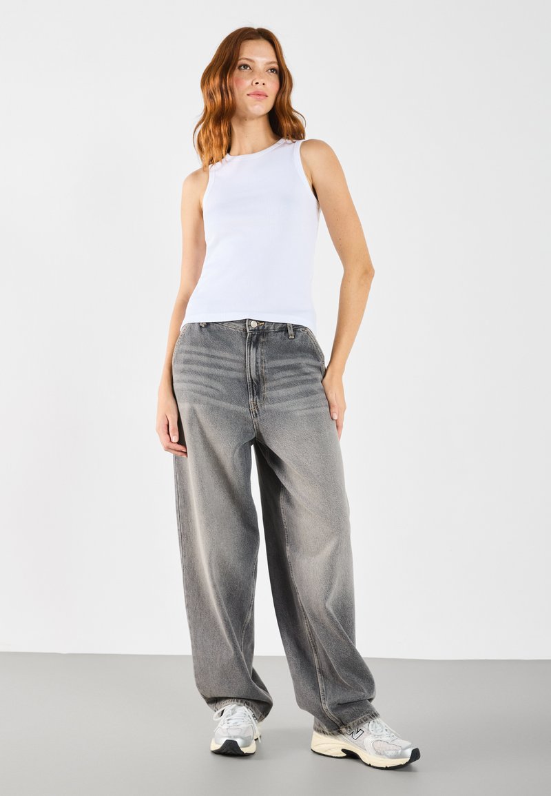 Hvit ribbet tanktop kombinert med vide grå bukser og grå sneakers. Antrekket har et enkelt design og er behagelig å bruke.