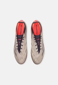 Crampons de football gris clair avec une tige texturée, lacets noirs et accents rouges sur la semelle intérieure et le talon, présentant un design élégant.