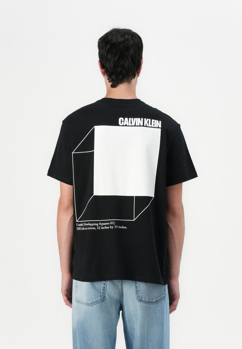 Juodas medvilninis marškinėliai su dideliu baltu geometriniu dizainu ant nugaros ir tekstu "CALVIN KLEIN" viršuje. Klasikinis kirpimas, trumpomis rankovėmis.