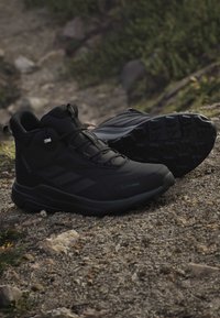 Μαύρα παπούτσια πεζοπορίας Adidas Terrex σε πετρώδη μονοπάτια με ορατή υφή στη σόλα, σχεδιασμένα για εξωτερικούς χώρους και όλες τις καιρικές συνθήκες.
