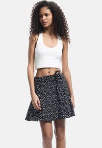 Un top court blanc avec un col rond associé à une jupe noire à motif floral et un détail de taille nouée.