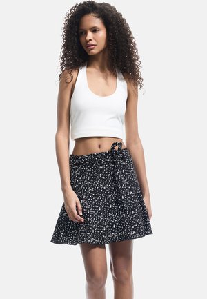 Top corto blanco con escote redondo combinado con una falda negra con un patrón floral y un detalle de cintura atada.