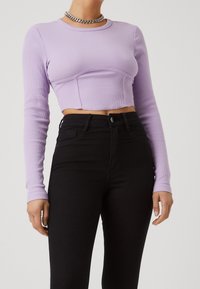 Ljuslila ribbat långärmad crop top med en åtsittande design, i kombination med högmidjade svarta jeans. Toppen har en rundad halsringning.