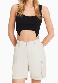 Top corto negro de canalé con escote redondo y detalle de corte, combinado con pantalones cortos cargo beige que tienen bolsillos laterales y un ajuste relajado.