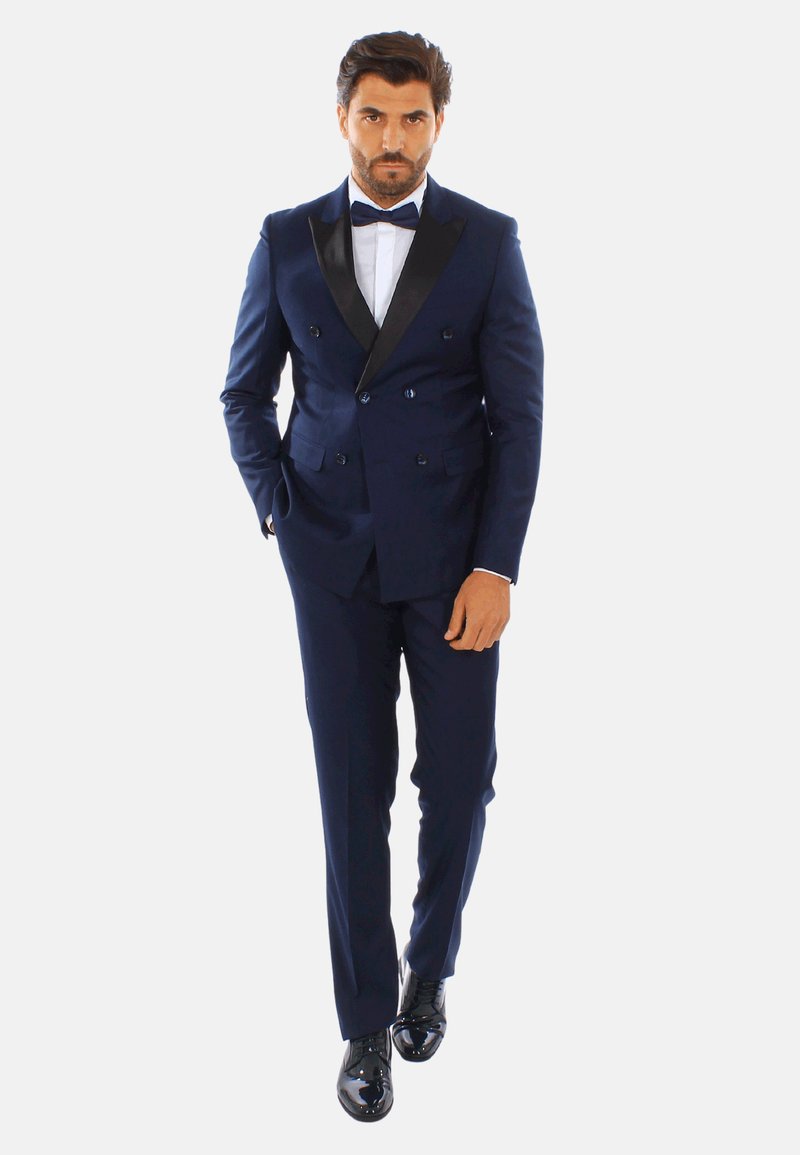 Tuxedo doppiopetto blu navy con revers in satin, camicia bianca e papillon nero. Scarpe eleganti nere lucide completano l'outfit.