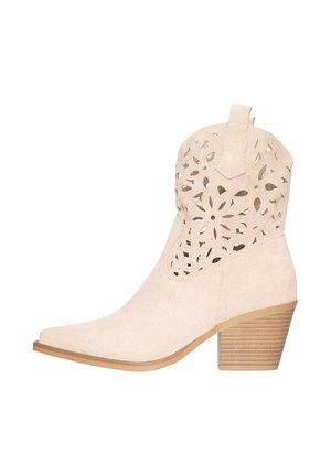 Stivaletto alla caviglia in camoscio beige con punta appuntita, motivo floreale traforato sulla parte superiore, linguetta, tacco a blocco impilato e suola color cuoio.