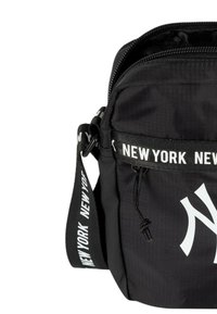 Borsa a tracolla in nylon nero con chiusura a zip, caratterizzata da una cintura bianca "New York" audace e un grande logo bianco sul davanti. Superficie testurizzata.