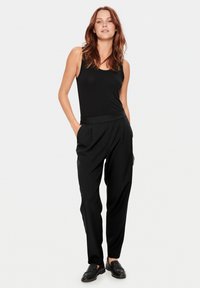 Un débardeur noir associé à un pantalon noir taille haute avec des plis. Tissu lisse avec une coupe décontractée, complété par des chaussures noires à enfiler.