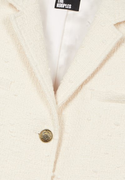 Blazer blanc texturé avec un col cranté, une fermeture à bouton unique doré, et une doublure satinée lisse.