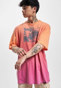 T-skjorte med kort erme, i gradient som går fra oransje til rosa, med et palme-motiv i midten. Mykt stoff og avslappet passform.
