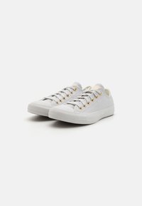 Valged kanva sneakerid madala ülemise osaga, millel on kuldsed silmad, tekstuuriga materjal ja kummist tallad mustriga tallaga.