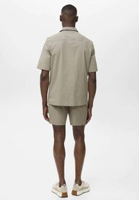 Lys khaki kort�ærmet skjorte og matchende shorts, lavet af glat stof. Casual design med en afslappet pasform, parret med cremefarvede sneakers.