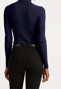 Ribbad mörkblå polotröja i kombination med högmidjade svarta jeans som har vanliga fickor och ett stilrent svart bälte.