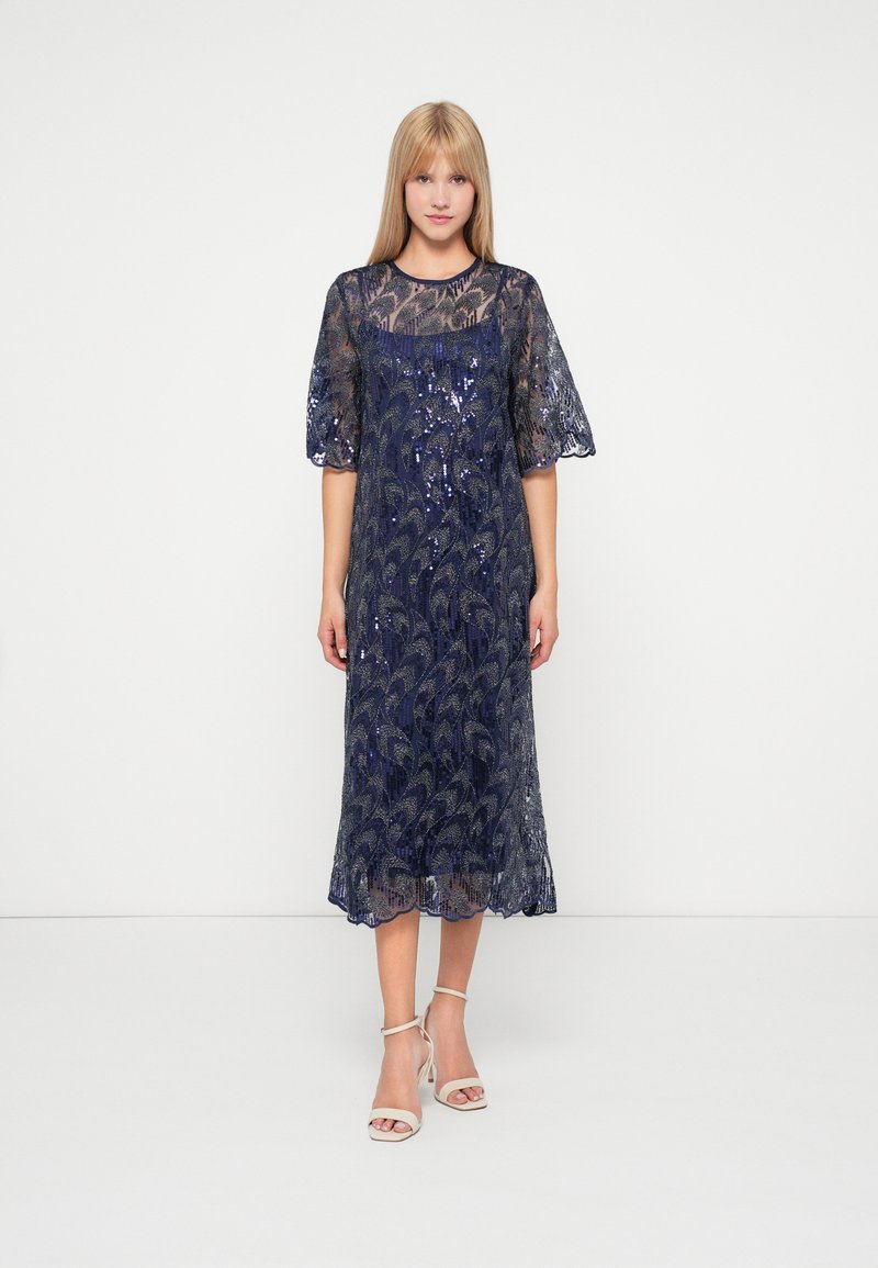 Robe en dentelle navy avec des sequins, manches courtes bouffantes et ourlet festonné. Elle présente un corsage ajusté avec une jupe fluide, créant une silhouette élégante.