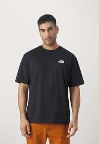 Black cotton t-shirt with short sleeves, round neckline, and a white logo on the left chest. Simple, relaxed fit design.