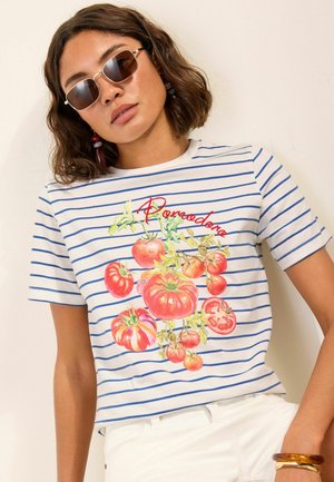 Kvinde iført rektangulære solbriller og en hvid t-shirt med blå striber og en farverig tomatplantegrafik med teksten "Pomodoro".