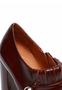 Scarpa in vernice bordeaux con punta appuntita, dettagli testurizzati sulla parte anteriore e tacco alto e spesso. Fodera interna liscia.