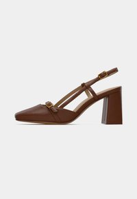Escarpin slingback en cuir marron avec bout pointu, bride ajustable et talon carré. Détail d'une petite boucle en or.