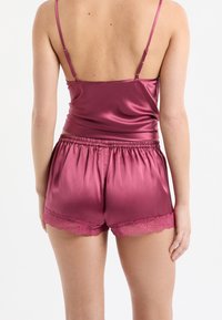 Satijnen pyjamaset in bordeauxrood met een aangesloten top met verstelbare bandjes en korte broek met een kanten rand aan de zoom.