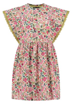 Barn iført en kort blomsterkjole med flæseærmer, som holder i kanten og går fremad i gule sandaler mod en ensfarvet baggrund.