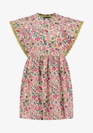 Barn iført en kort blomsterkjole med flæseærmer, som holder i kanten og går fremad i gule sandaler mod en ensfarvet baggrund.