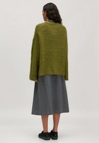 Grüner übergroßer Strickpullover mit flauschiger Textur, getragen über einem langen grauen Rock. Das Outfit beinhaltet dunkle Schuhe und wird von hinten betrachtet.
