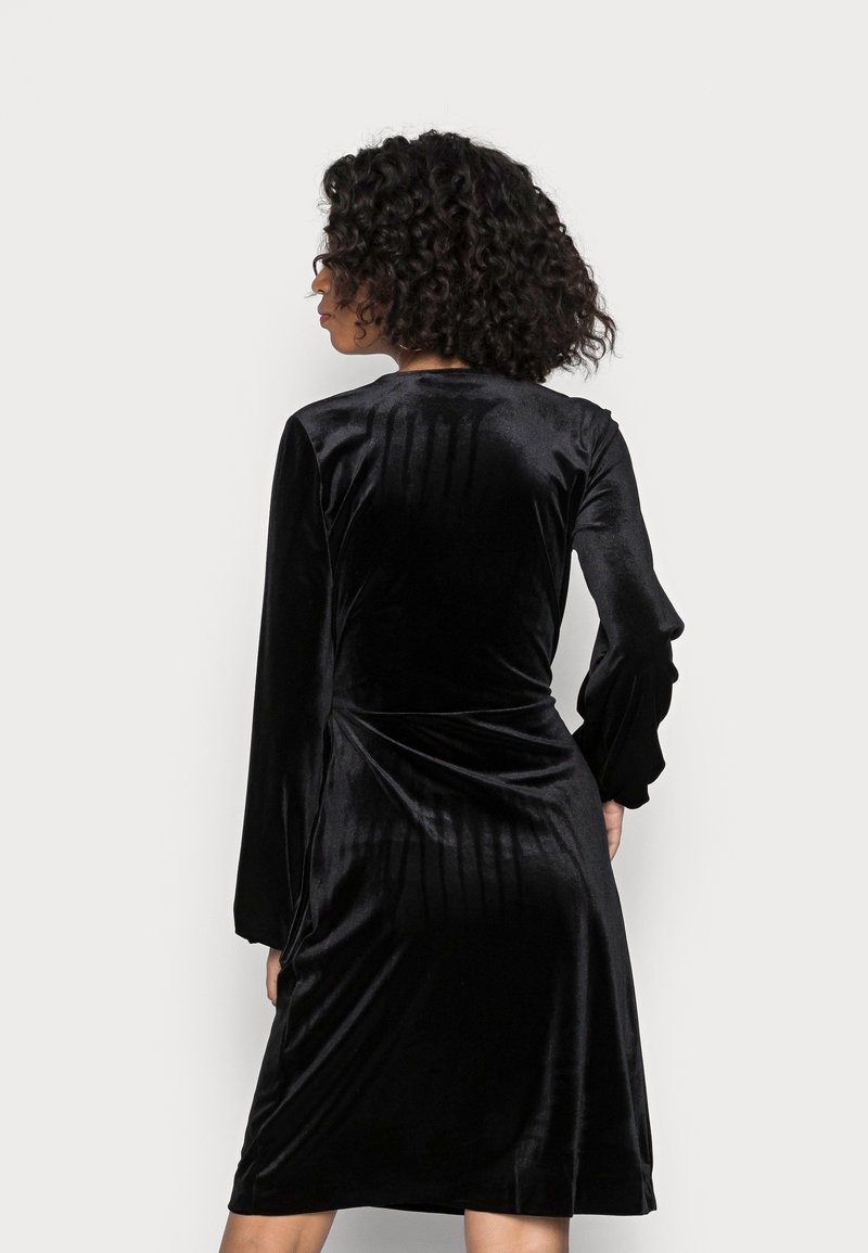 Schwarzes Samtkleid mit langen, gerafften Ärmeln, tailliertem Oberteil und einem Rock, der gerade über dem Knie endet. Glatte Textur mit einem leichten Schimmer.