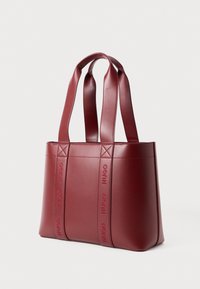 Borsa tote in pelle rossa con due manici larghi e logo "HUGO" in rilievo sulle cinghie verticali frontali, su uno sfondo bianco.