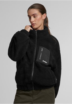 Schwarze Fleecejacke mit hohem Kragen, durchgehendem Reißverschluss und einer Vordertasche. Hat eine weiche Textur und einen gerippten Saum. Markenname auf der Tasche.