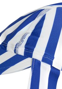 Kék és fehér csíkos anyagú sapka, lekerekített tetejével, amelyen a varrások mentén látható a varrás, és elegáns kialakítással rendelkezik.