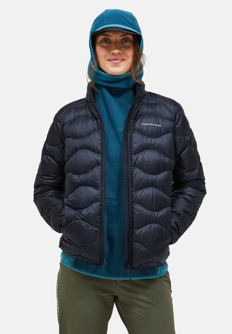 Zwarte pufferjack met een gewatteerd patroon, rits aan de voorkant en elastische manchetten. Draagt over een teal fleece top, in combinatie met olijfgroene broek.